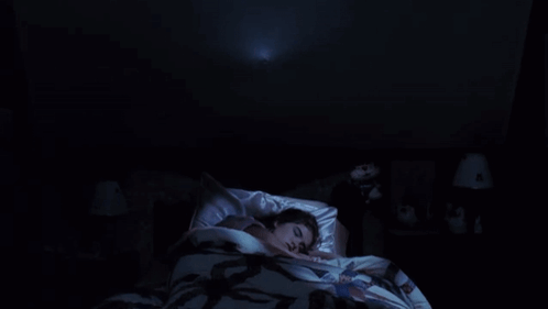 A Woman Is Laying In Bed With A Ghost Coming Out Of The Ceiling Above Her . GIF