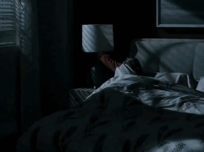 A Woman Is Laying In Bed With A Lamp On The Nightstand Next To Her . GIF
