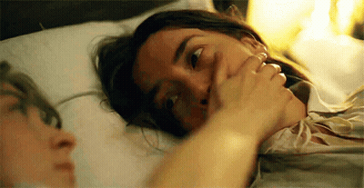 A Woman Is Laying In Bed With A Man Covering Her Mouth With Her Hand . GIF
