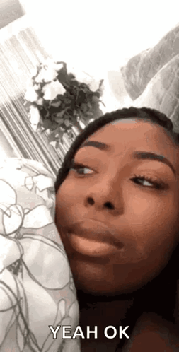 A Woman Is Laying In Bed With A Pillow And Making A Funny Face While Saying Yeah Ok . GIF