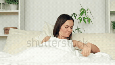 A Woman Is Laying In Bed With Her Arms Outstretched And The Word Shutterstock Is On The Bottom GIF