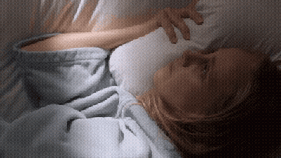 A Woman Is Laying In Bed With Her Hand On Her Forehead GIF