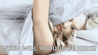 A Woman Is Laying In Bed With The Words `` When Will Youuu Be Here '' Written On The Bottom Of The Image . GIF