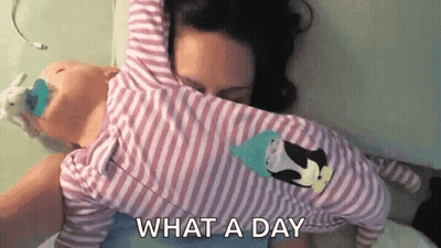 A Woman Is Laying On A Bed Holding A Baby In Her Arms And Says `` What A Day '' . GIF