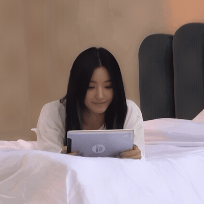 A Woman Is Laying On A Bed Holding A Hp Tablet GIF