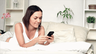 A Woman Is Laying On A Bed Using A Cell Phone GIF
