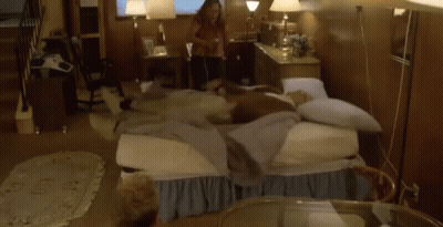 A Woman Is Laying On A Bed With A Bunch Of Pillows Flying Around Her . GIF
