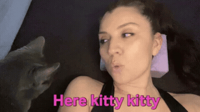 A Woman Is Laying On A Bed With A Cat Looking At Her And Says `` Here Kitty Kitty '' . GIF