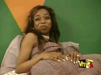 A Woman Is Laying On A Bed With A Pillow And A Blanket On Her Stomach . GIF