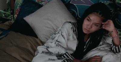 A Woman Is Laying On A Bed With A Pillow And Looking At The Camera . GIF