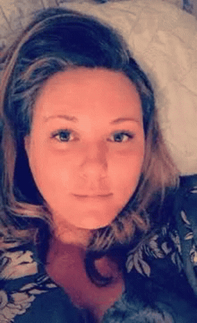 A Woman Is Laying On A Bed With A Pillow In Her Lap And Looking At The Camera . GIF