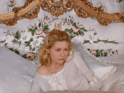 A Woman Is Laying On A Bed With Flowers On The Headboard GIF
