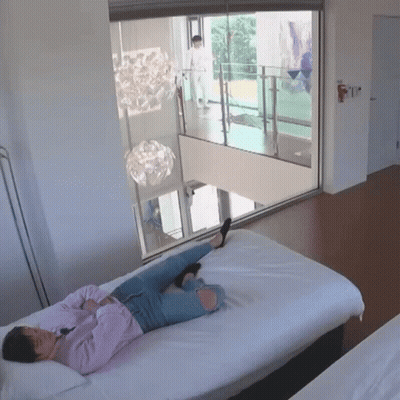 A Woman Is Laying On A Bed With Her Legs Crossed In Front Of A Window GIF