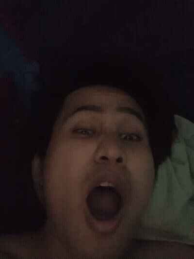 A Woman Is Laying On A Bed With Her Mouth Open And Her Tongue Sticking Out . GIF