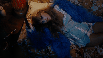 A Woman Is Laying On A Couch Wearing A Blue Fur Coat GIF