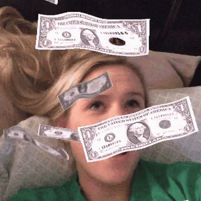 A Woman Is Laying On A Couch With Money Falling On Her Head GIF