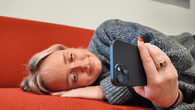 A Woman Is Laying On A Red Couch Looking At Her Cell Phone GIF