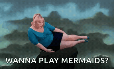 A Woman Is Laying On A Rock With The Words `` Wanna Play Mermaids ? '' Written Below Her . GIF