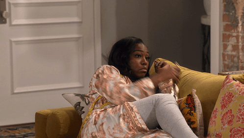 A Woman Is Laying On A Yellow Couch With A Pillow That Says R On It GIF