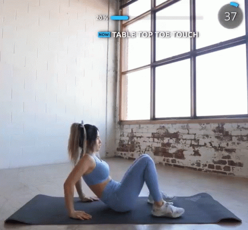 A Woman Is Laying On A Yoga Mat With The Words Now Table Top Toe Touch On The Screen GIF