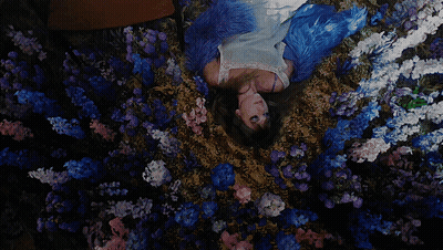 A Woman Is Laying On Her Back In A Field Of Blue And Pink Flowers GIF