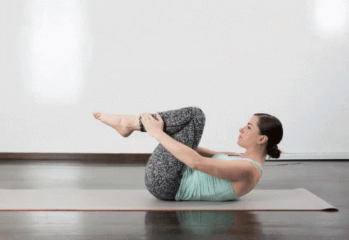 A Woman Is Laying On Her Back On A Yoga Mat With Her Legs Crossed GIF