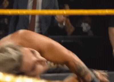 A Woman Is Laying On The Ground In A Wrestling Ring While A Man In A Suit Watches . GIF
