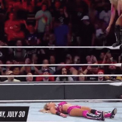 A Woman Is Laying On The Ground In A Wrestling Ring While A Man Jumps Over Her . GIF