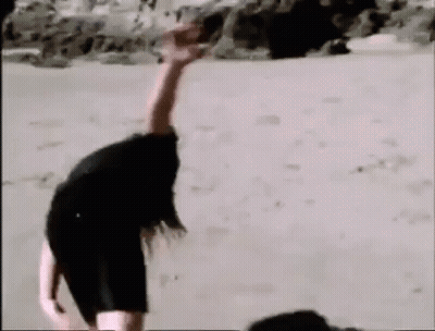 A Woman Is Laying On The Sand With Her Arms Outstretched . GIF
