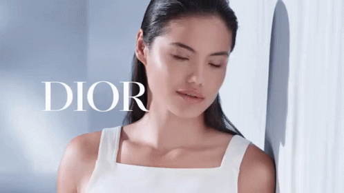 A Woman Is Leaning Against A Wall With Her Eyes Closed And The Word Dior Behind Her GIF
