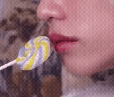 A Woman Is Licking A Colorful Lollipop From Her Lips . GIF