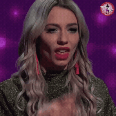 A Woman Is Licking Her Finger While Wearing Red Earrings And A Green Top GIF