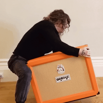 A Woman Is Lifting An Orange Amplifier On Her Knees GIF