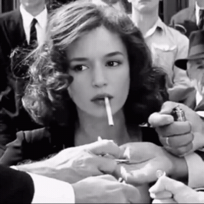 A Woman Is Lighting A Cigarette In A Crowd Of People GIF