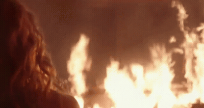 A Woman Is Looking At A Large Fire In The Dark . GIF