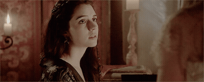 A Woman Is Looking At Another Woman In A Room With A Candle In The Background GIF