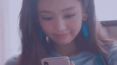 A Woman Is Looking At Her Phone And Smiling While Wearing Earrings . GIF