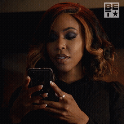 A Woman Is Looking At Her Phone With A Be T Logo In The Background GIF