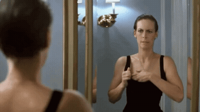 A Woman Is Looking At Her Reflection In A Mirror . GIF
