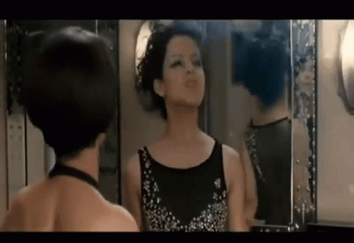 A Woman Is Looking At Herself In A Mirror . GIF