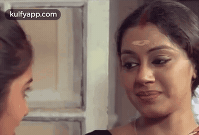 A Woman Is Looking At Herself In A Mirror . GIF