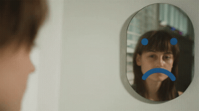 A Woman Is Looking At Herself In A Mirror With A Sad Face Drawn On It GIF