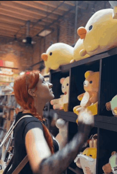 A Woman Is Looking At Stuffed Animals On A Shelf GIF