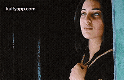 A Woman Is Looking Out Of A Window And Holding Her Hand To Her Chest . GIF