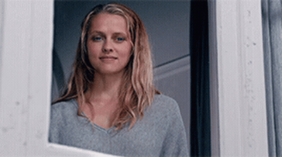A Woman Is Looking Out Of A Window And Smiling . GIF