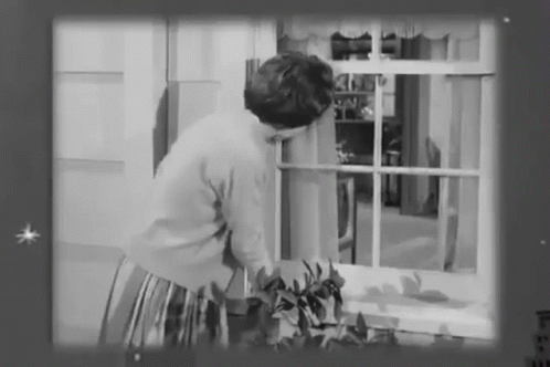 A Woman Is Looking Out Of A Window In A Black And White Photo . GIF