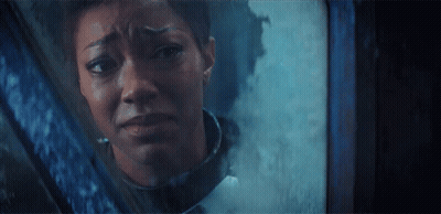 A Woman Is Looking Out Of A Window With A Sad Look On Her Face GIF