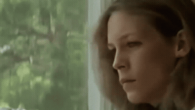 A Woman Is Looking Out Of A Window With A Serious Look On Her Face . GIF