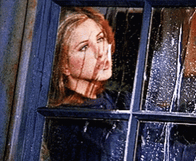 A Woman Is Looking Out Of A Window With Rain Drops On The Window GIF