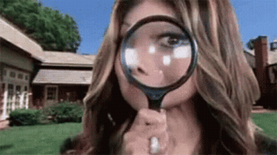 A Woman Is Looking Through A Magnifying Glass To Her Face . GIF
